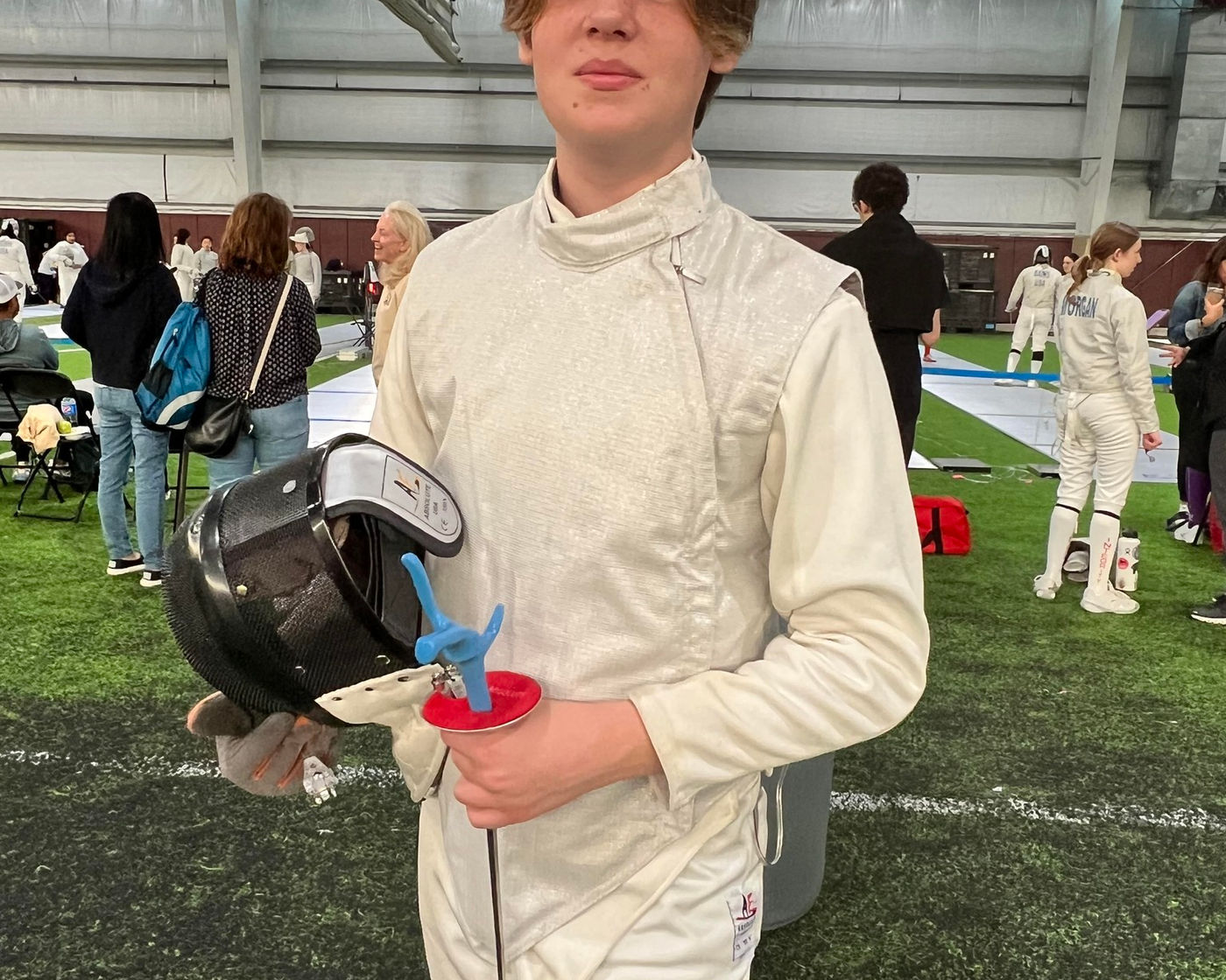 A young NJFA fencer holding their mask and weapon